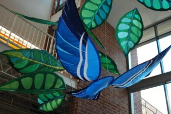 Large blue and green fabric leaves suspended from the ceiling in an indoor art installation